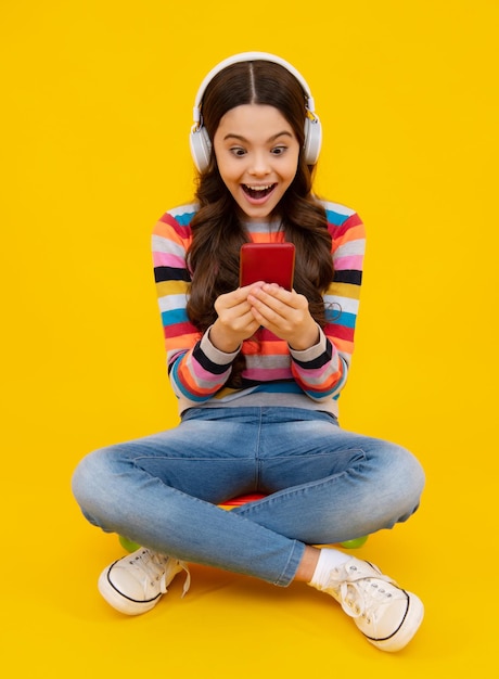 Niño adolescente asombrado sosteniendo teléfono celular Retrato de primer plano de una linda adolescente usando una aplicación web de celular de teléfono móvil aislada sobre un fondo de color amarillo brillante vivo y vibrante