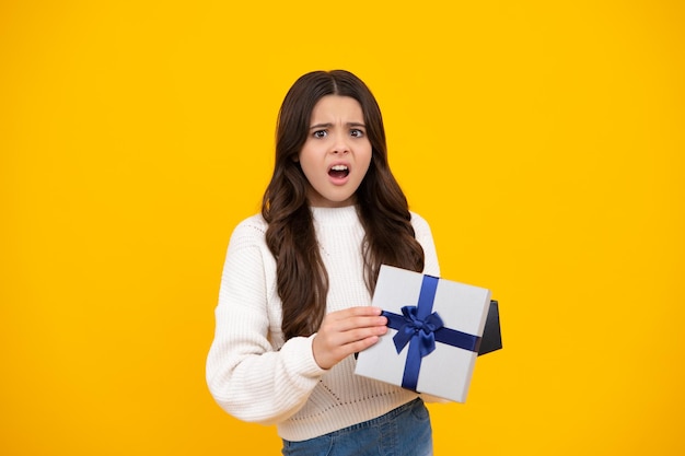 Niño adolescente con caja de regalo sobre fondo amarillo aislado Regalo para cumpleaños de niños Caja de regalo de Navidad o Año Nuevo Cara enfadada emociones molestas de niña adolescente