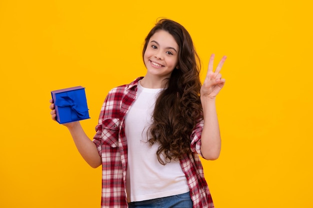 Niño adolescente en camisa con caja de regalo sobre fondo amarillo aislado Regalo para cumpleaños de niños Adolescente feliz emociones positivas y sonrientes de niña adolescente