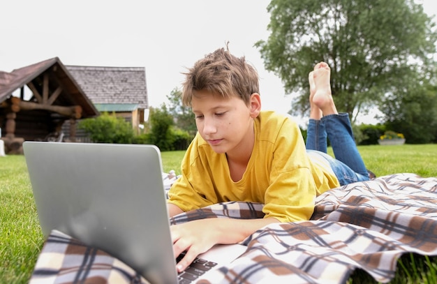 Niño adolescente escribiendo en su computadora portátil en el parque Niño estudiando o jugando a juegos de computadora al aire libre en el prado