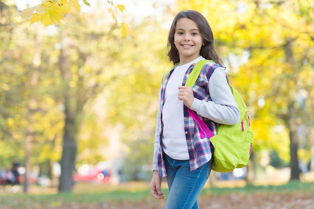 Niño adolescente feliz en bosque otoñal con hermosa naturaleza estacional llevar mochila escolar, infancia.