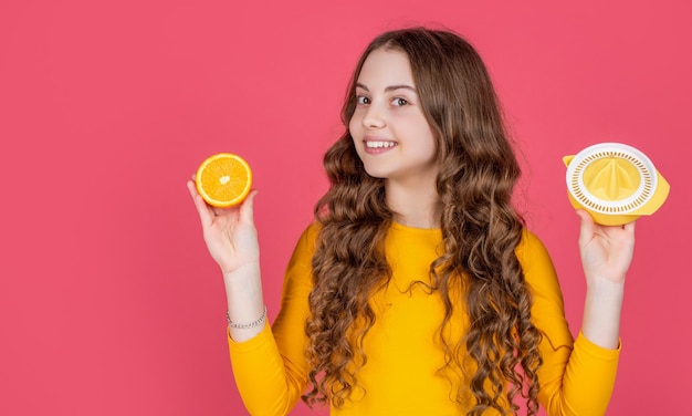 Niño adolescente feliz sostenga naranja y exprimidor sobre fondo rosa