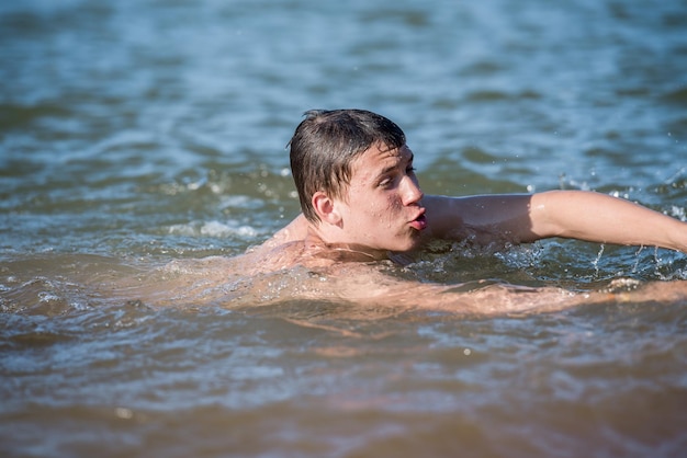 Un niño adolescente nada en un chorro de agua, un concepto de vacaciones en la playa