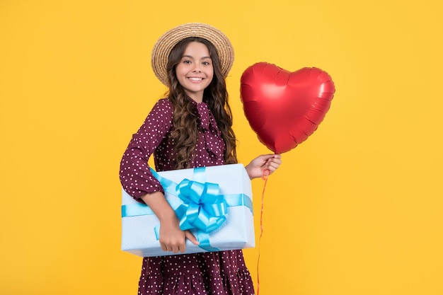 Niño adolescente sonriente con globo de corazón rojo y caja de regalo sobre fondo amarillo