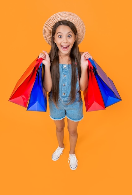 Niño adolescente sorprendido con bolsas de compras sobre fondo amarillo de cuerpo entero