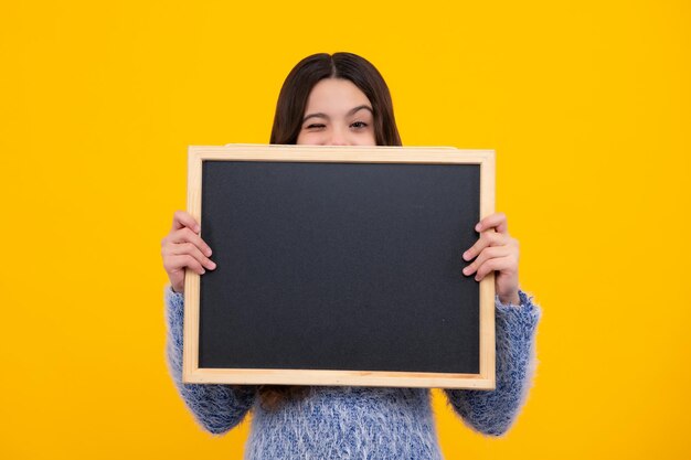 Foto niño adolescente sosteniendo una pizarra en blanco para el mensaje aislado en un fondo amarillo espacio de copia de pizarra de texto vacío maqueta