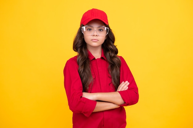 Foto niño adolescente trabajador vistiendo overoles gorra roja y gafas protectoras studio shot retrato aislado sobre fondo amarillo