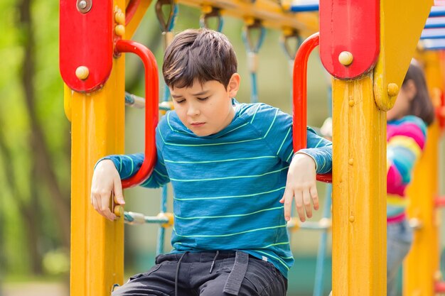 Un niño adolescente triste y aburrido sentado en un patio de recreo colorido en verano