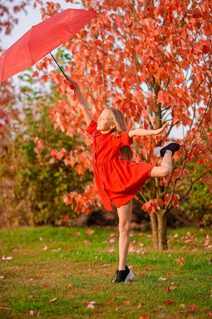 Niño adorable feliz con sombrilla roja en otoño