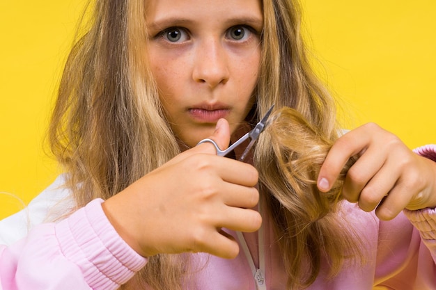 Niño adorable niña peluquera cortando cabello largo y rubio con tijeras metálicas en amarillo