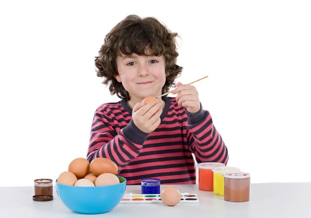 Niño adorable que adorna los huevos de Pascua en un fondo blanco