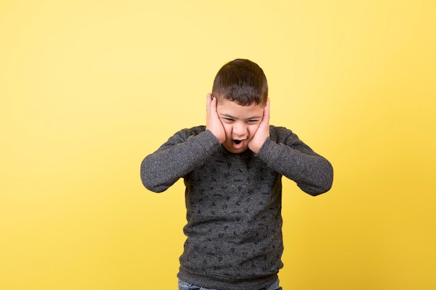 niño adorable en ropa casual de pie y tapándose los oídos.