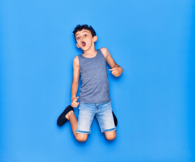 Un niño adorable con ropa informal saltando sobre un fondo azul aislado