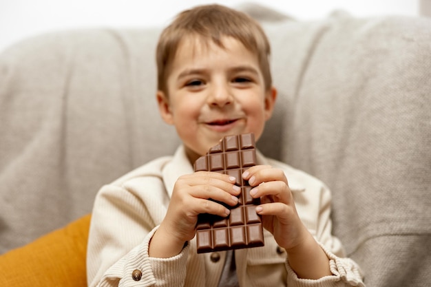 Un niño adorable sentado en el sofá de casa y comiendo una barra de chocolate Niño y dulces Confitería de azúcar Niño disfruta de un delicioso postre Niño en edad preescolar con ropa informal Emoción positiva