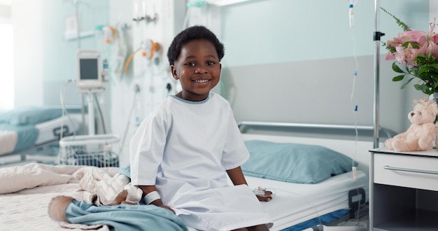 Niño africano enfermo hospital y cama con cara sonrisa y descanso para la recuperación del tratamiento quirúrgico o atención médica Niño paciente feliz y retrato para relajarse sentado y clínica para la rehabilitación