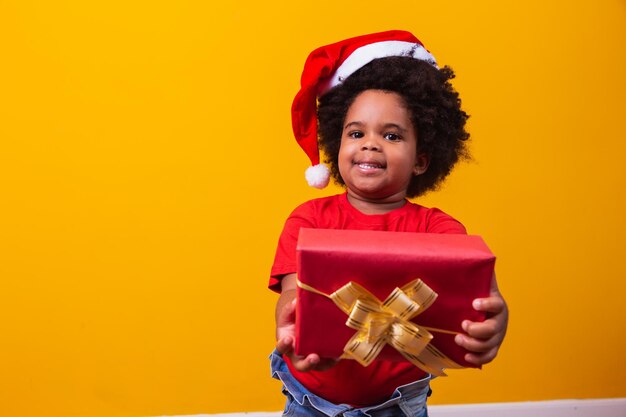 Niño afro sonriente con sombrero rojo de Santa Claus con regalo de Navidad en la mano. Concepto de navidad.