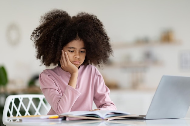 Niño afroamericano aburrido que sufre mientras hace la tarea