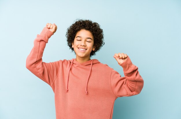 Niño afroamericano aislado celebrando un día especial, salta y levanta los brazos con energía.