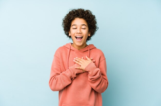 Niño afroamericano aislado riendo manteniendo las manos en el corazón, concepto de felicidad.