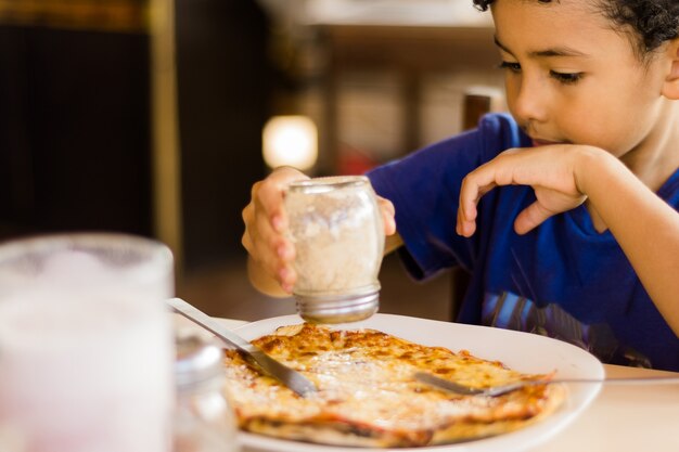 Niño afroamericano feliz comiendo pizza.