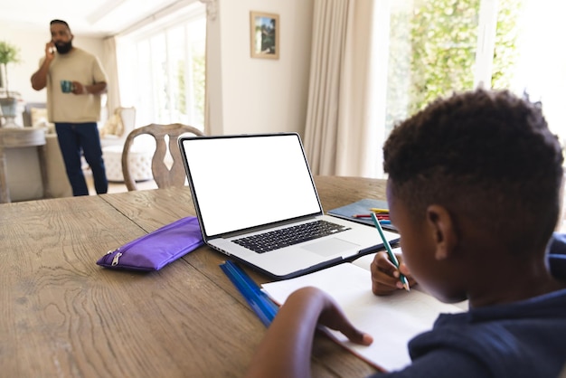 Niño afroamericano sentado en la mesa, usando una computadora portátil con espacio de copia para la lección en línea