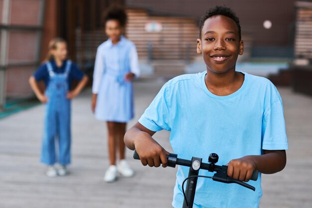 Nino afroamericano sonriente con camiseta azul claro montando scooter electrico Foto Premium