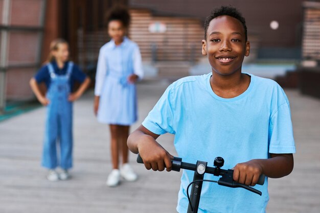 Niño afroamericano sonriente con camiseta azul claro montando scooter eléctrico