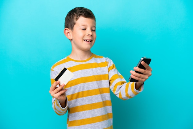Niño aislado de fondo azul comprando con el móvil con tarjeta de crédito