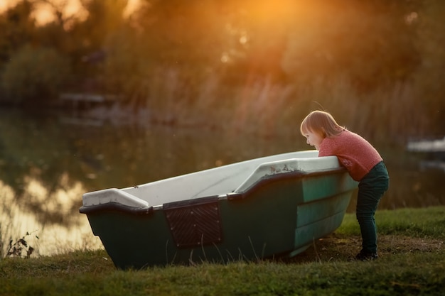 Niño al aire libre se encuentra cerca de un bote de madera en el lago