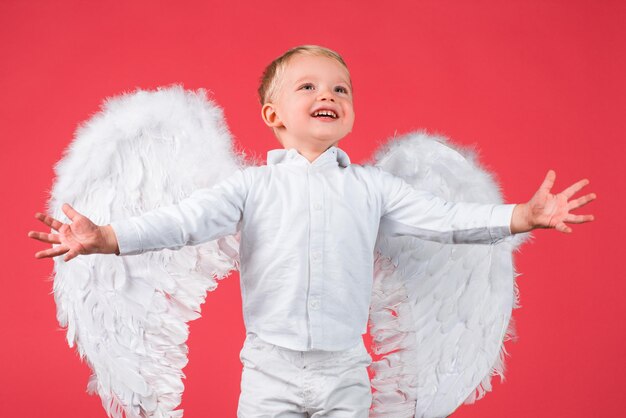 Niño con alas de ángel aislado en rojo.