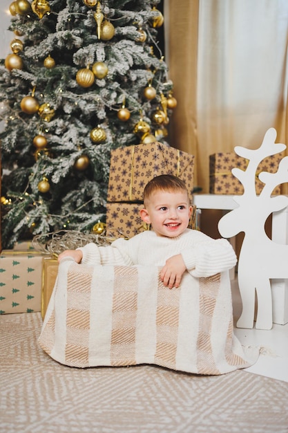 Un niño alegre de 23 años está de pie cerca de un árbol de Navidad rodeado de guirnaldas y la Navidad presenta el concepto de un cuento de Navidad una fiesta para niños pequeños árbol de Navidad