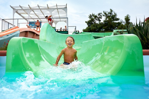 Foto el niño alegre baja por el tobogán de agua verde a la piscina levantando salpicaduras vacaciones de verano