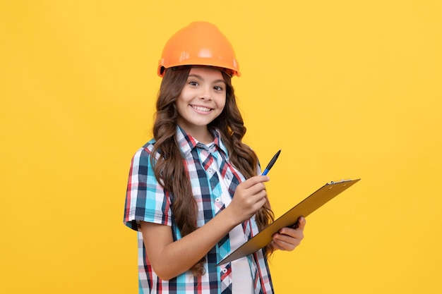 Niño alegre en casco de construcción haciendo notas en el portapapeles tomando notas