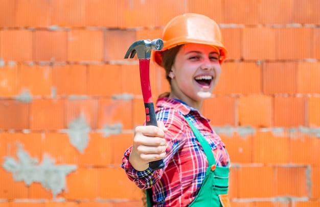 Foto niño alegre en casco sostenga martillo carpintería y concepto de carpintería niño adolescente usando herramientas de construcción y reparación de herramientas de martillo reparador niña pequeña reparando en taller enfoque selectivo