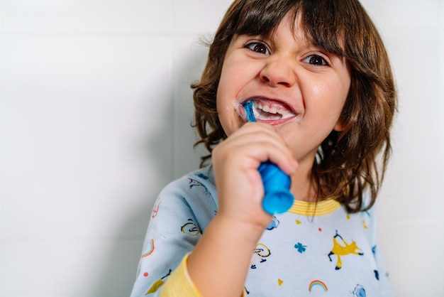 Niño alegre cepillándose los dientes en pijama antes de acostarse