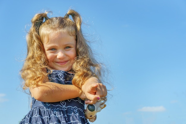 Niño alegre contra el cielo azul. niña de 4 años señala con el dedo a la cámara.