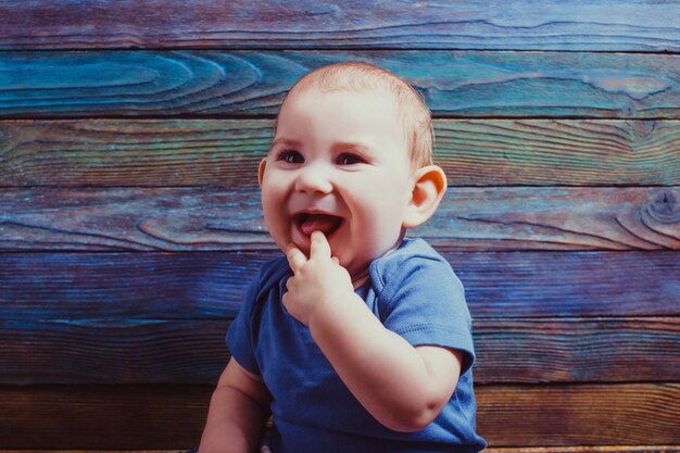 Niño alegre con el dedo en la boca sobre un fondo de madera de color