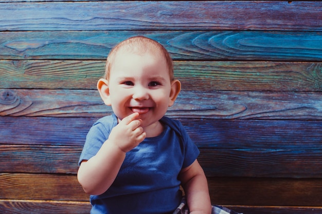 Niño alegre con el dedo en la boca sobre un fondo de madera de color