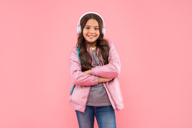 Niño alegre escuchando música en auriculares con mochila escolar con música de fondo rosa