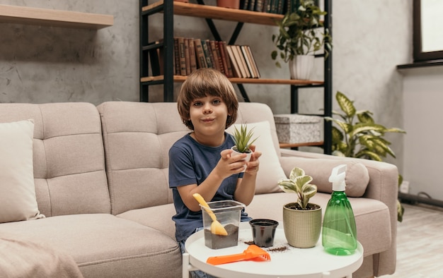 Un niño alegre está sentado en un sofá en una habitación y huele una planta de aloe en una maceta