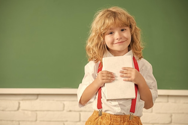 Niño alegre en estudio de pajarita en la clase de la escuela que muestra la sabiduría del espacio de copia del cuaderno