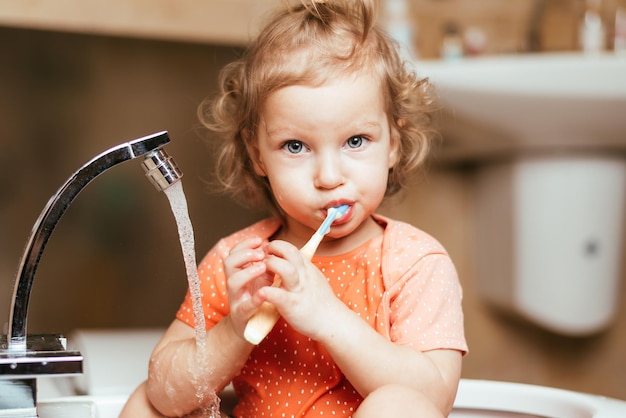 Un niño alegre y feliz se cepilla los dientes por la mañana en el baño