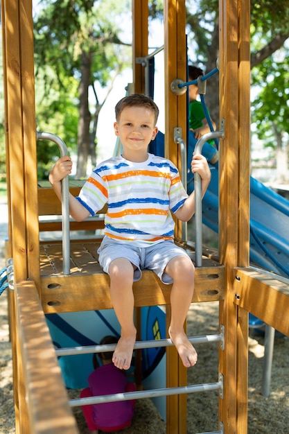 Un niño alegre y feliz está sentado en la parte superior de un parque infantil con toboganes en el patio