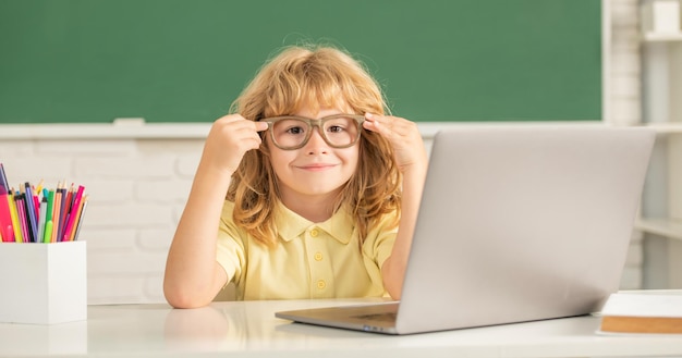 Niño alegre con gafas estudia en línea en la clase de la escuela con una computadora portátil en septiembre