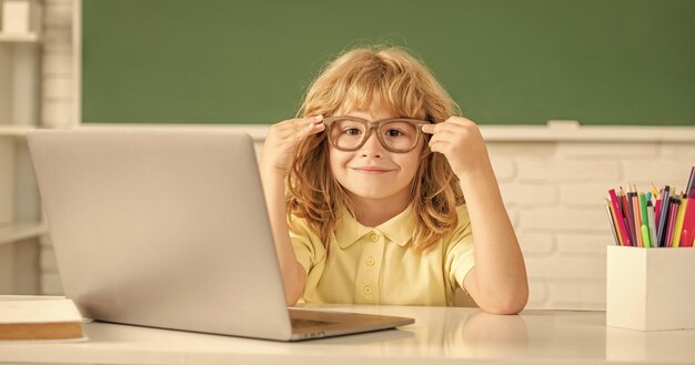 Niño alegre con gafas estudia en línea en la clase de la escuela con una computadora portátil en septiembre