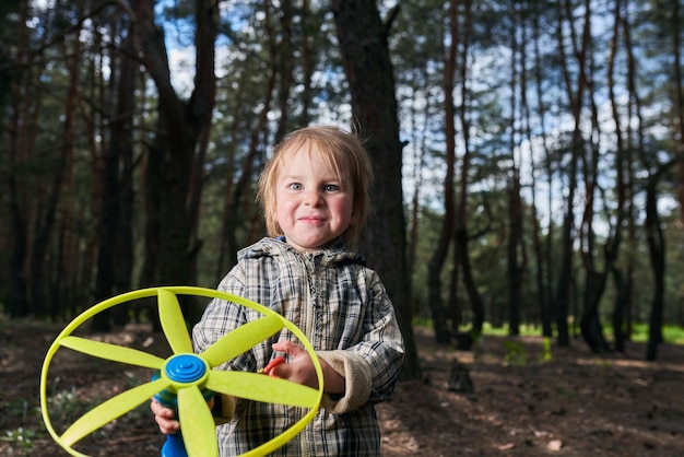 Un niño alegre jugando con una hélice de juguete en el bosque