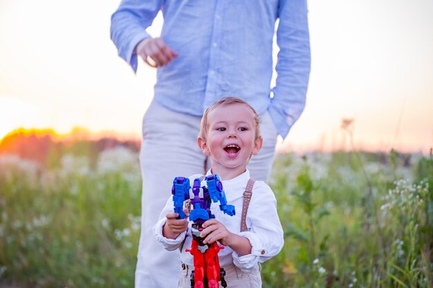 Niño alegre jugando con un robot en el campo y su padre cerca de él.