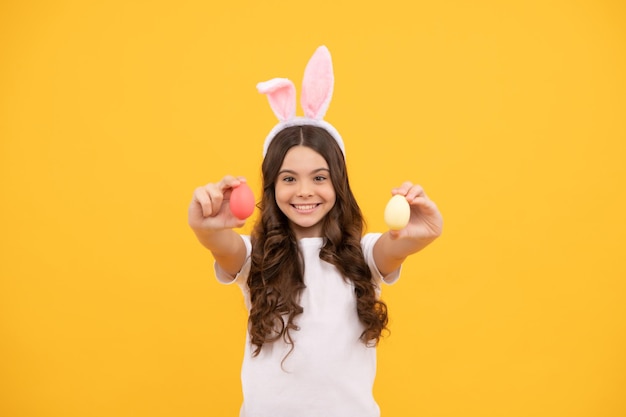 Niño alegre en orejas de conejo sostiene huevos sobre fondo amarillo felices pascuas