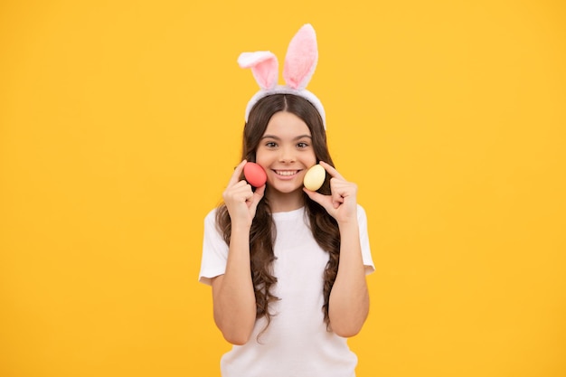 Niño alegre en orejas de conejo sostiene huevos sobre fondo amarillo pascua