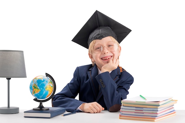 Niño alegre de primer grado con sombrero de estudiantes y anteojos grandes junto a cuadernos y globo Concepto de estudio y educación